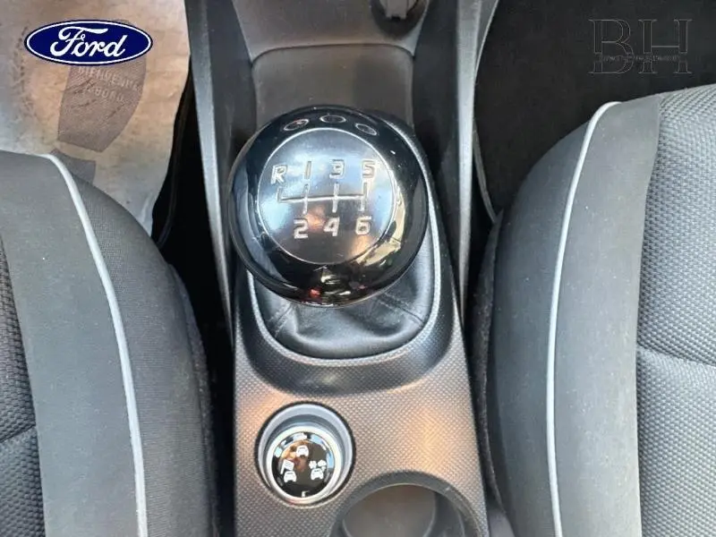Gros plan sur le levier de vitesses manuel noir et la console centrale entre les sièges tissu bi-color gris et noir d'une Fiat 500X argentée.