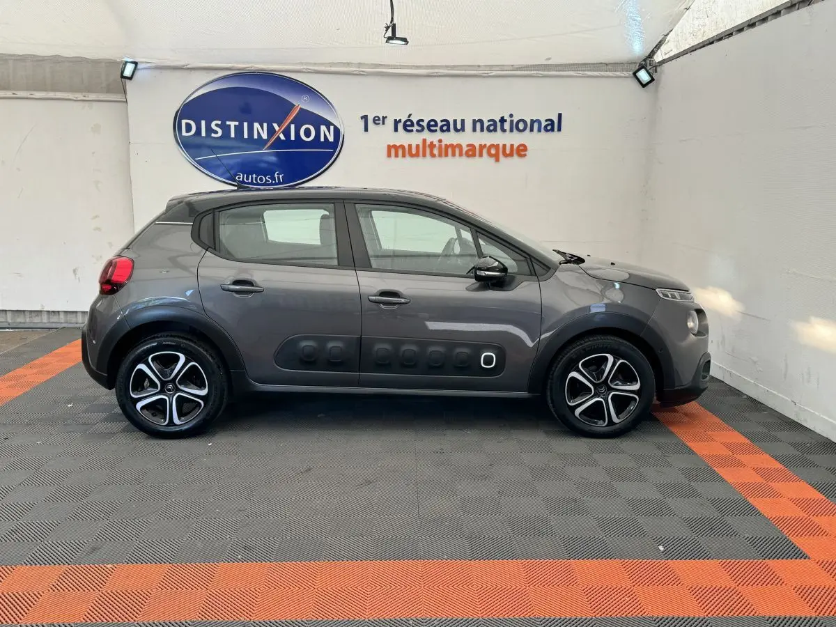 Vue de profil côté gauche d'une Citroën C3 gris foncé avec protections latérales noires et jantes alliage bicolores.