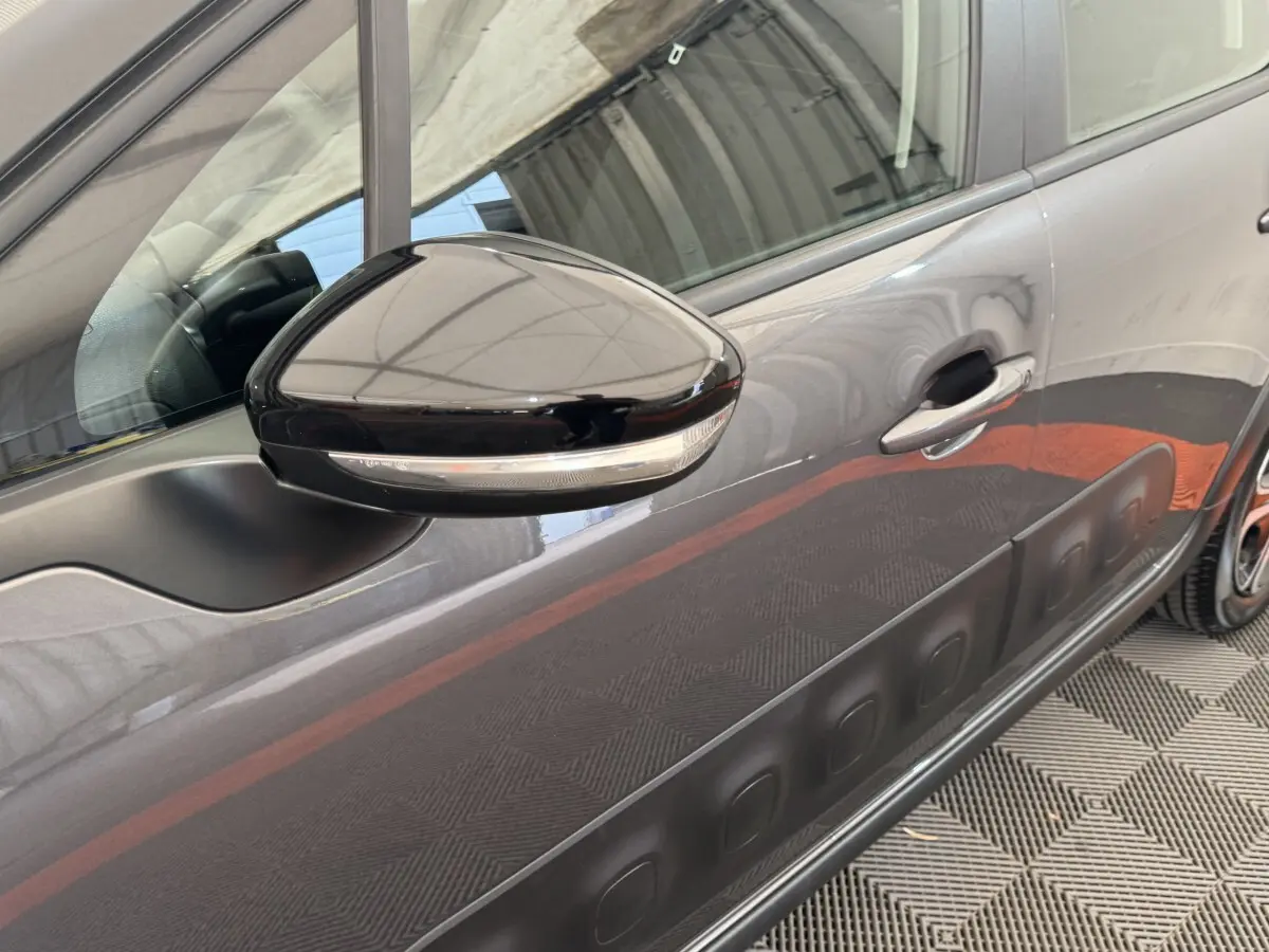 Gros plan sur le rétroviseur et la portière côté droit d'une Citroën C3 gris foncé avec protections latérales noires.