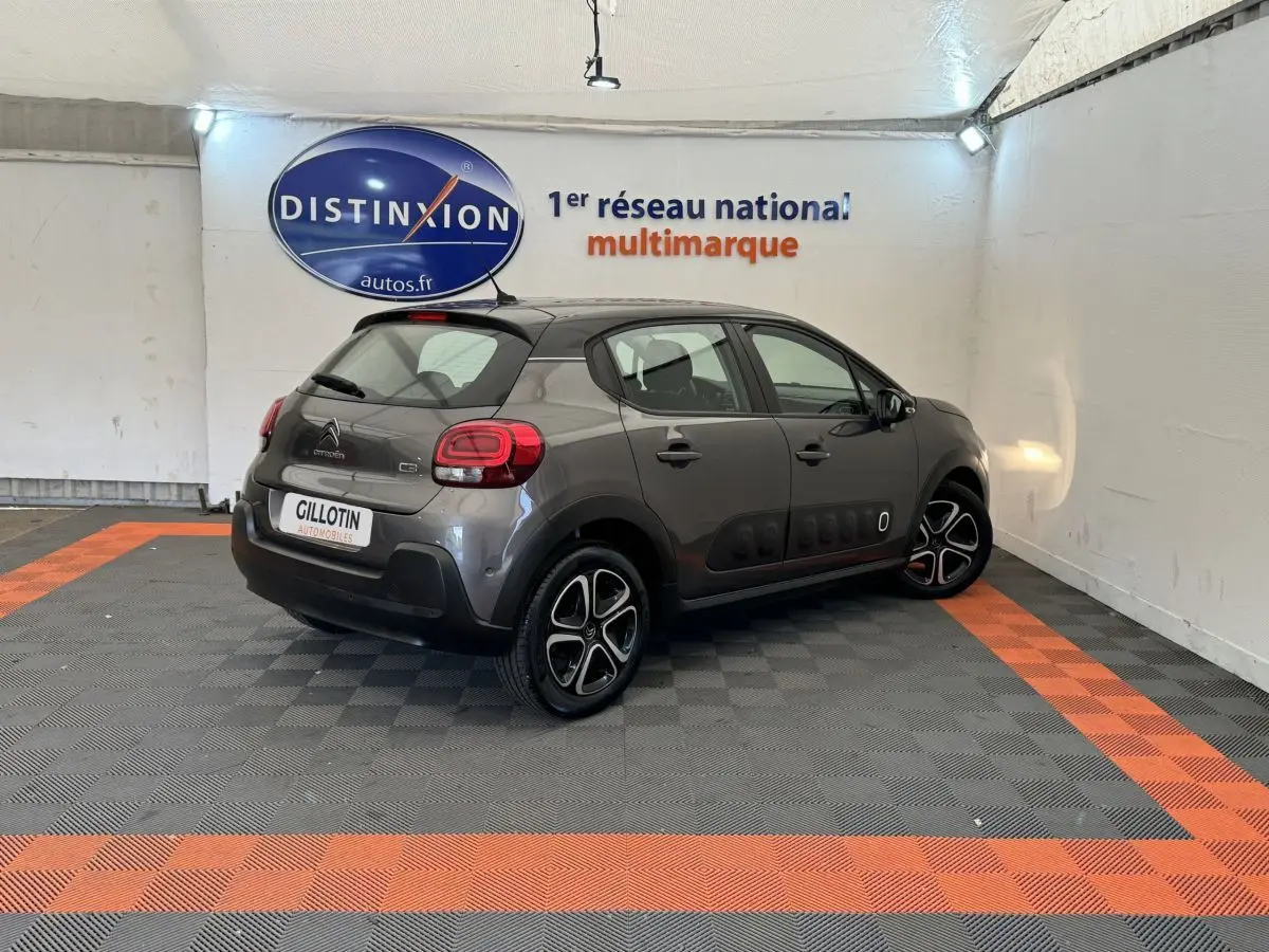 Citroën C3 gris foncé vue 3/4 arrière droit, avec protections latérales noires et jantes bicolores.