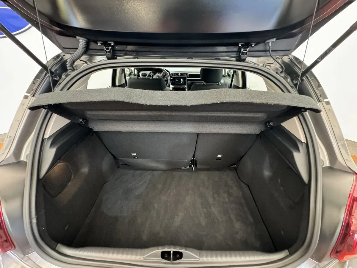 Coffre ouvert vu de l'arrière d'une Citroën C3 gris foncé, banquette arrière et tableau de bord visibles.
