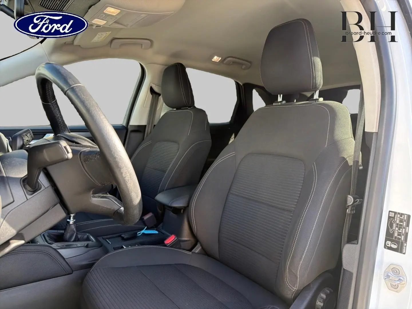 Vue intérieure côté conducteur du Ford Kuga blanc Glacier 2021, sièges sport noirs avec coutures contrastantes.
