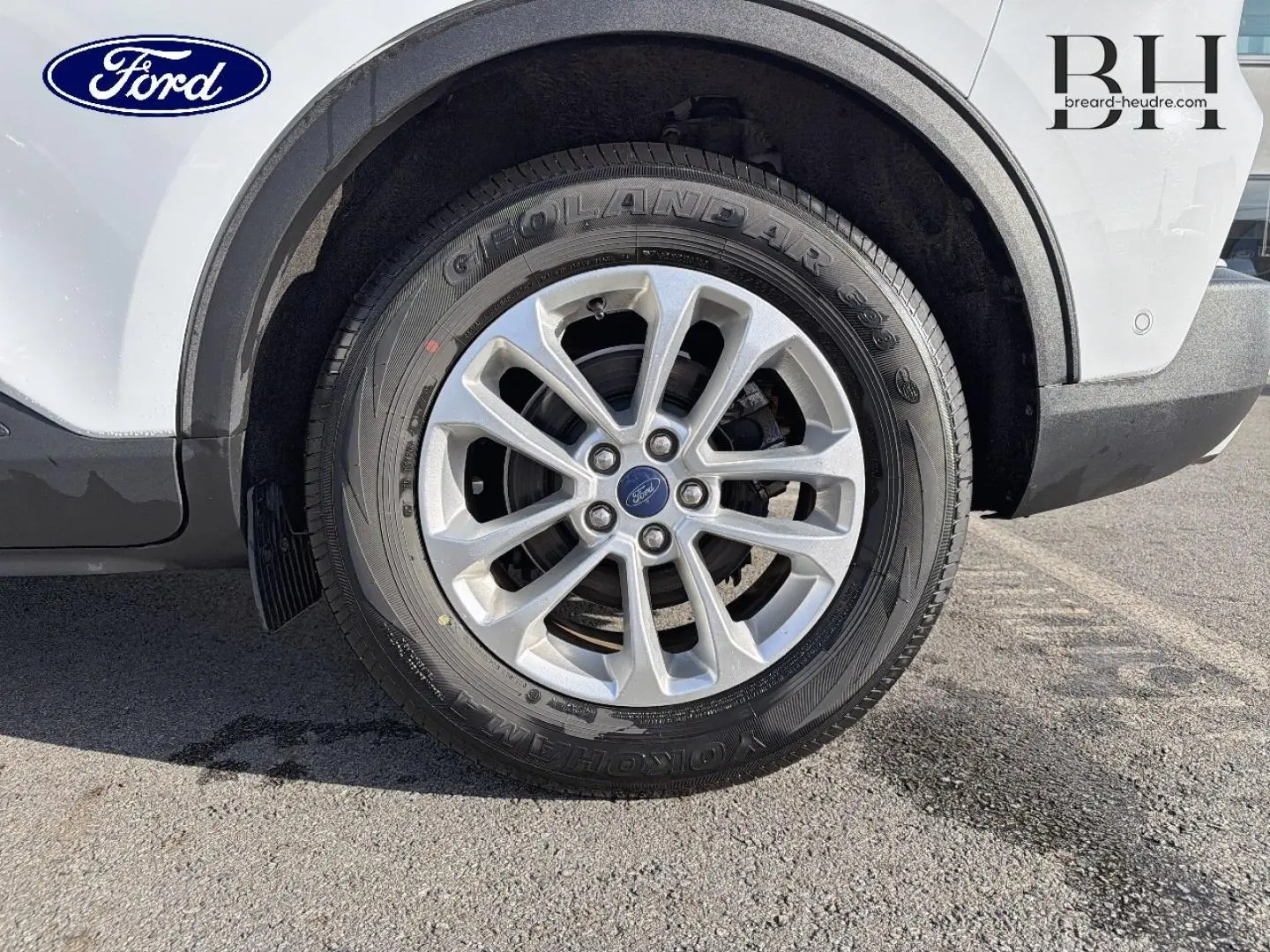 Gros plan sur la roue avant gauche avec jante alu du Ford Kuga blanc Glacier, montrant le pneu Yokohama et l'aile arrière.