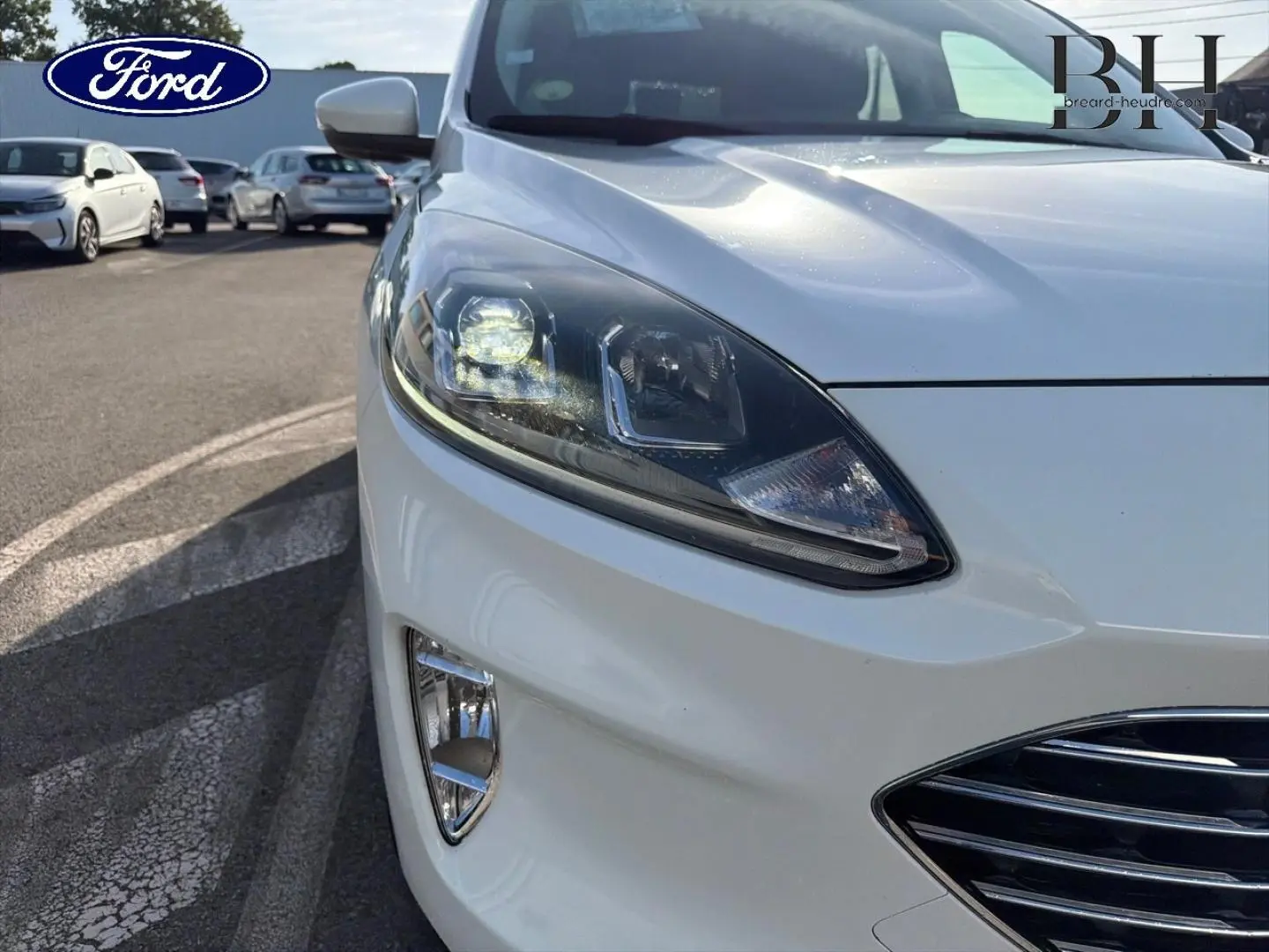 Gros plan sur l'avant droit du Ford Kuga blanc Glacier, mettant en valeur le phare LED et la calandre chromée.