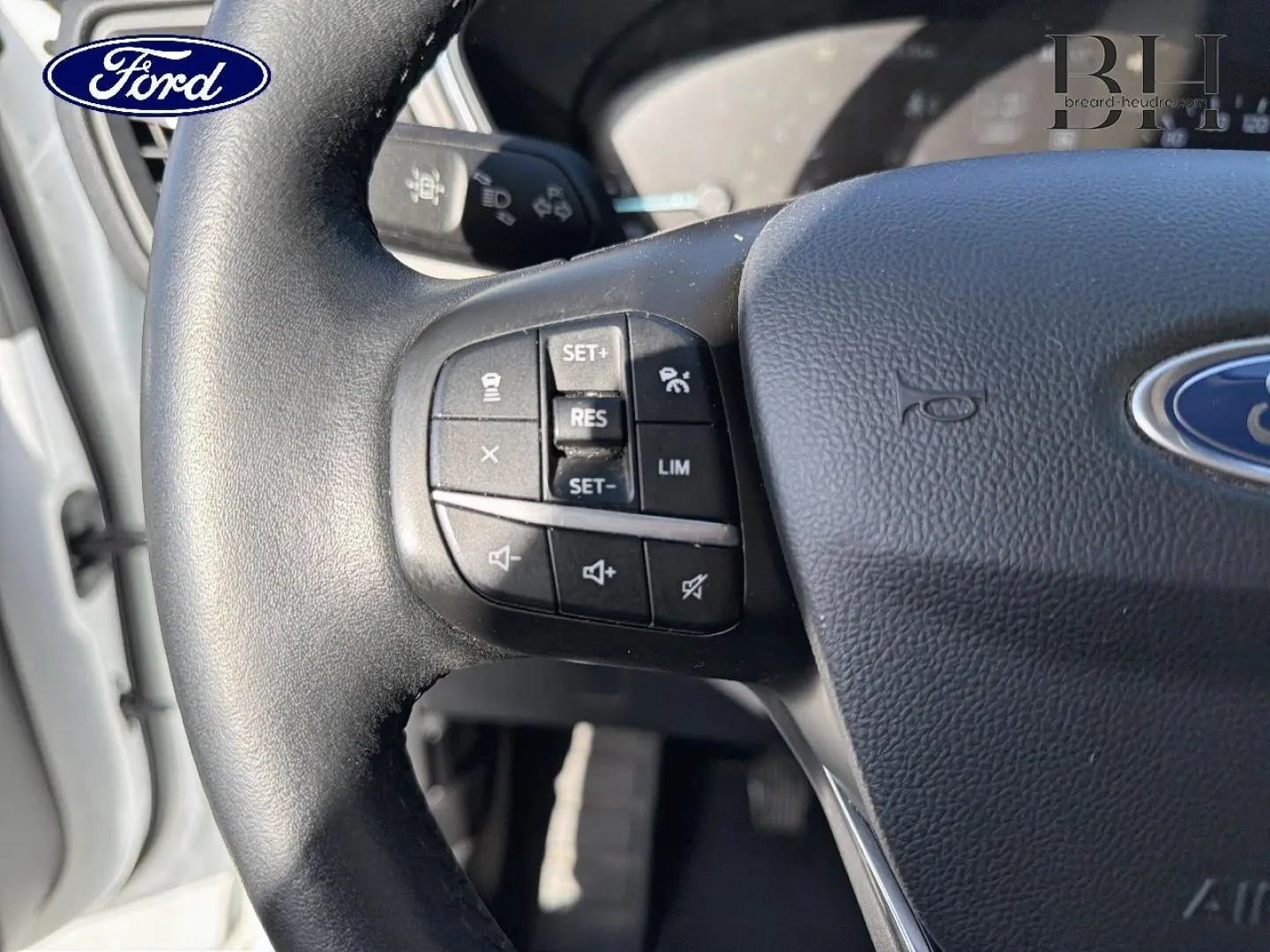 Gros plan sur le volant cuir multifonction noir du Ford Kuga blanc Glacier, avec commandes de régulateur et limiteur de vitesse.
