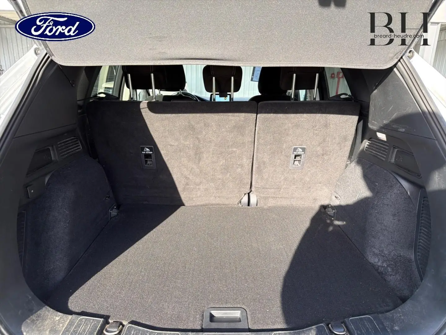 Coffre ouvert du Ford Kuga blanc Glacier 2021, montrant l'espace de chargement et la banquette arrière rabattable.