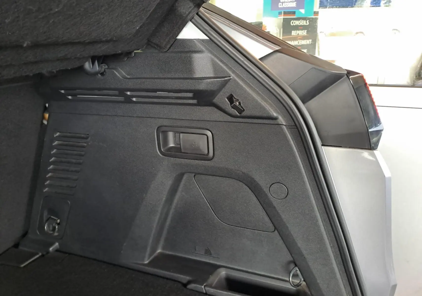 Détail intérieur du coffre côté droit du Peugeot 3008 gris Artense, montrant les rangements et finitions en plastique noir.