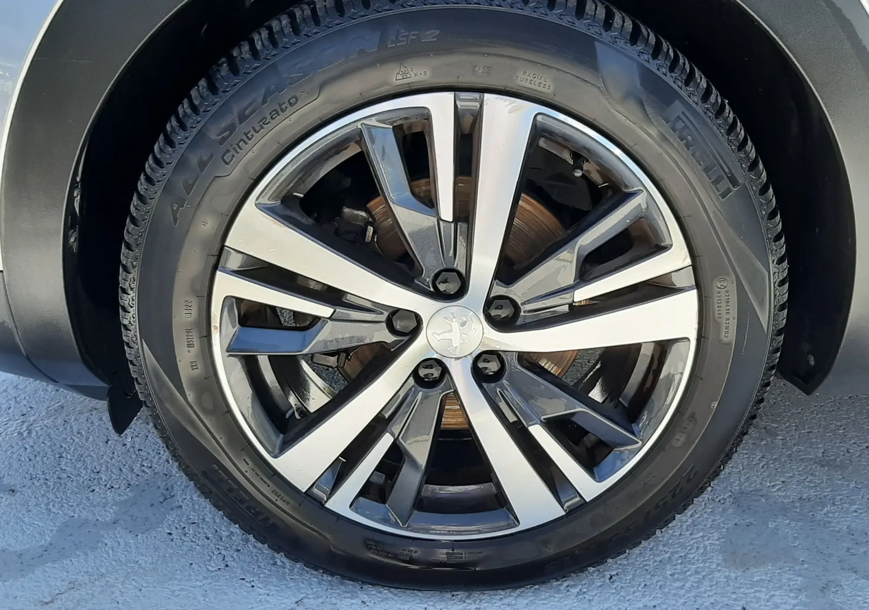 Gros plan sur la roue avant droite du Peugeot 3008 gris Artense avec jante alliage bicolore et logo lion central.