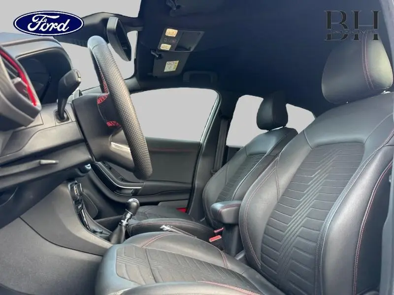 Intérieur avant du Ford Puma 2022, sièges en cuir noir avec surpiqûres rouges et volant sport visible côté conducteur.