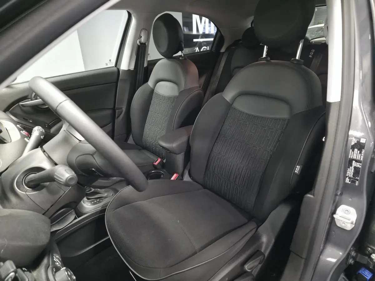 Intérieur de la Fiat 500X 2024 en gris, vue côté conducteur montrant sièges noirs avec monogramme FIAT et accoudoir central.
