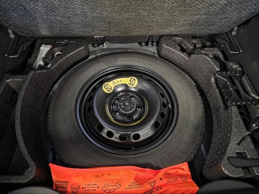 Gros plan sur la roue de secours noire dans le coffre d'une Fiat 500X 2024 gris, avec kit de sécurité orange visible.