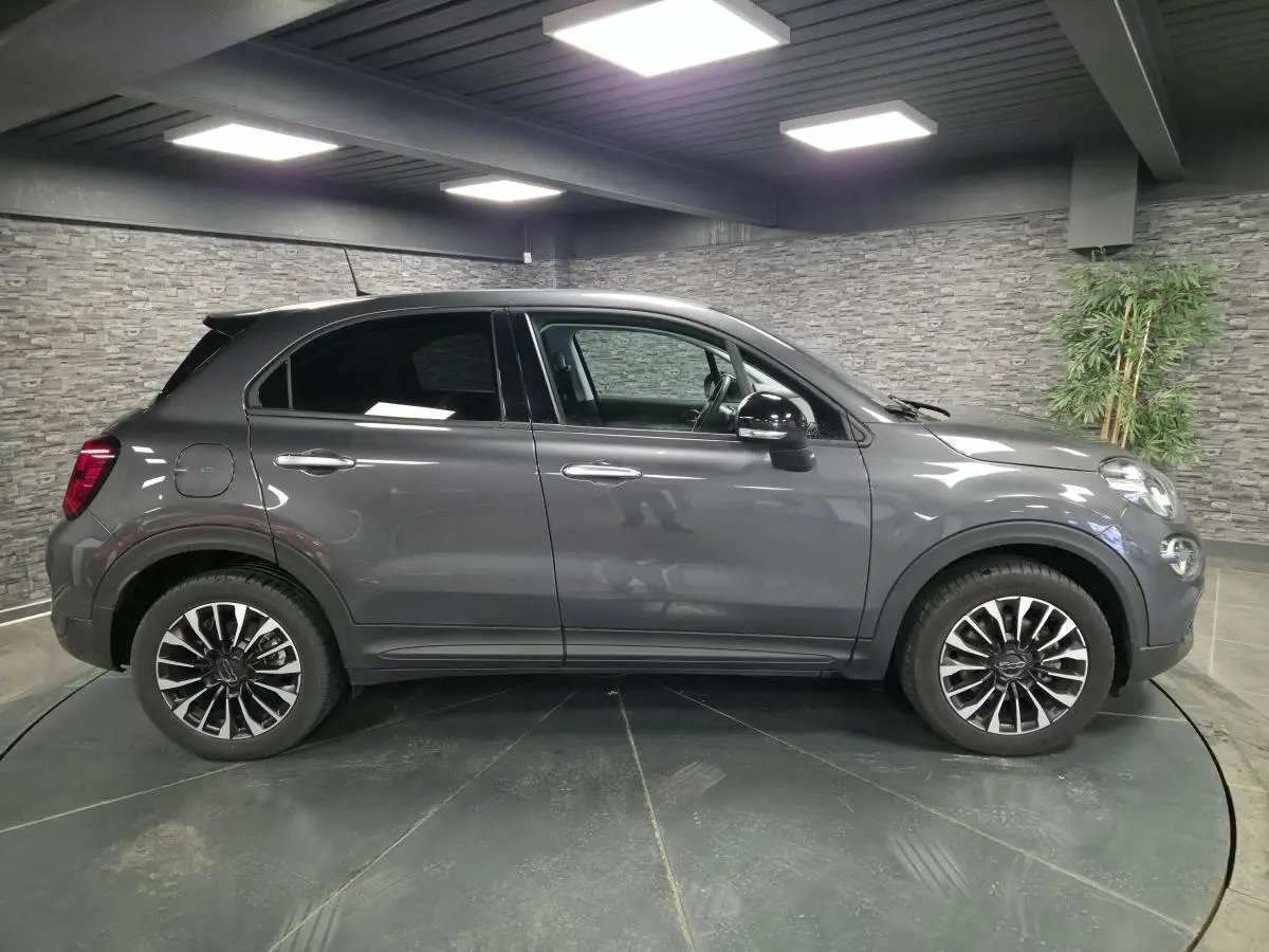 Profil droit d'un Fiat 500X gris métallisé 2024 avec jantes alliage 17 pouces et vitres surteintées dans un showroom.