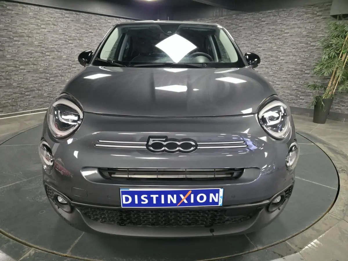Vue frontale d'une Fiat 500X 2024 gris métallisé avec logo 500 distinctif et projecteurs LED ronds allumés.