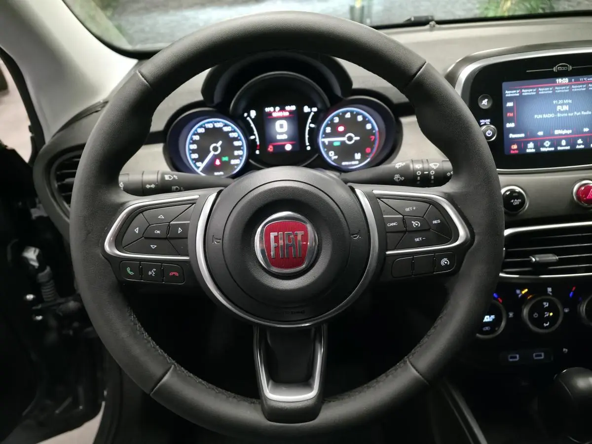 Vue rapprochée du volant noir de la Fiat 500X 2024 avec commandes intégrées et tableau de bord numérique éclairé.