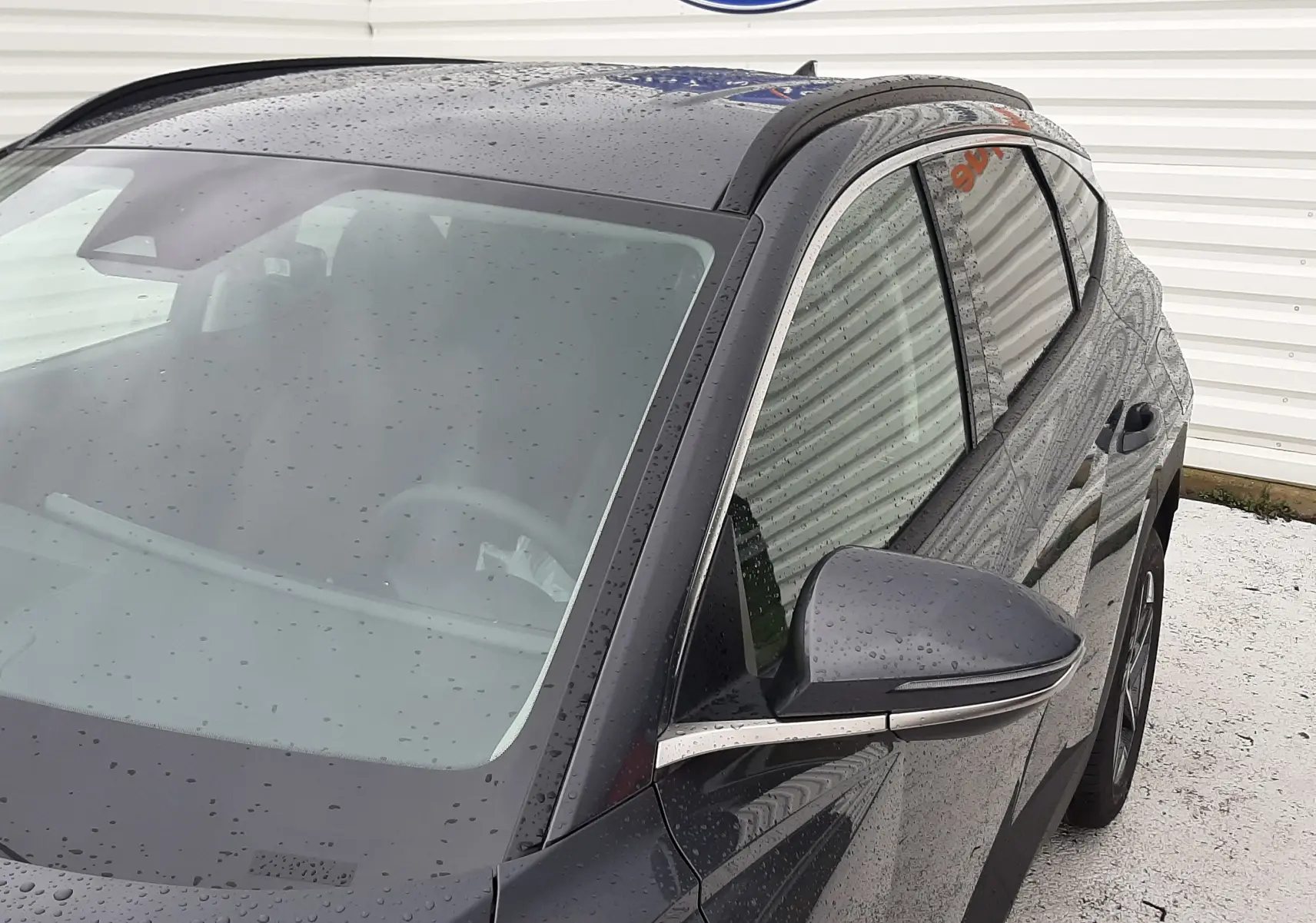 Vue 3/4 avant droit du Hyundai Tucson 2025 en gris Ecotronic, avec gouttes de pluie visibles sur la carrosserie.