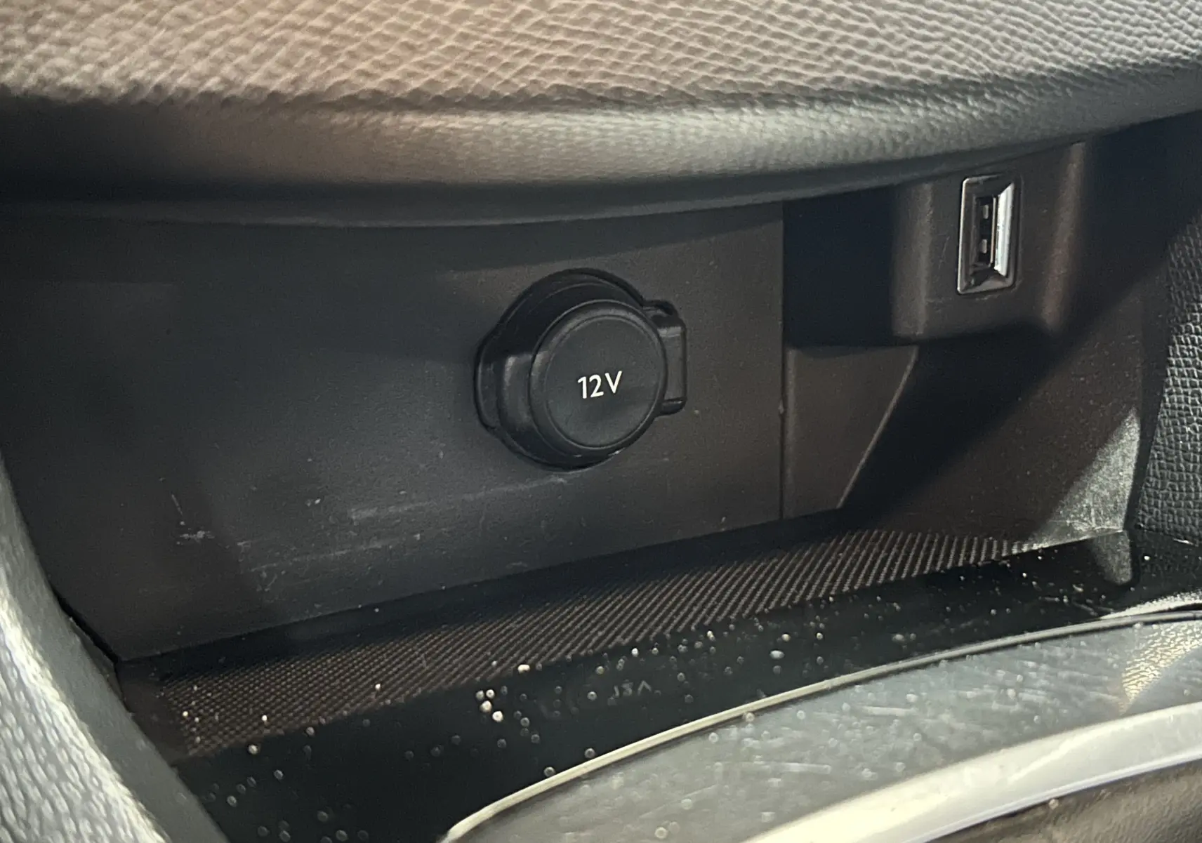 Prise 12V et port USB dans l'espace de rangement intérieur d'une Peugeot 308 SW noire, vue rapprochée.