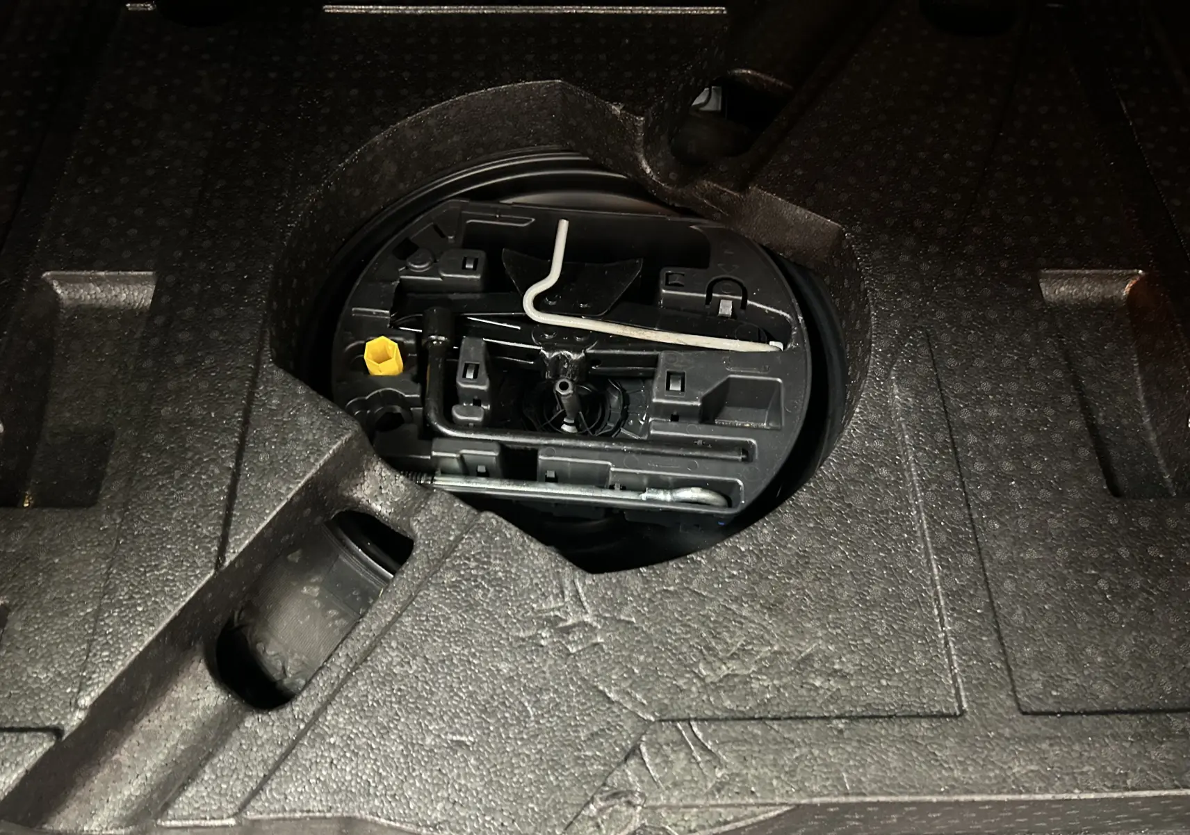 Gros plan sur le compartiment de rangement sous le plancher du coffre du Peugeot 308 SW noir, montrant les outils de bord.