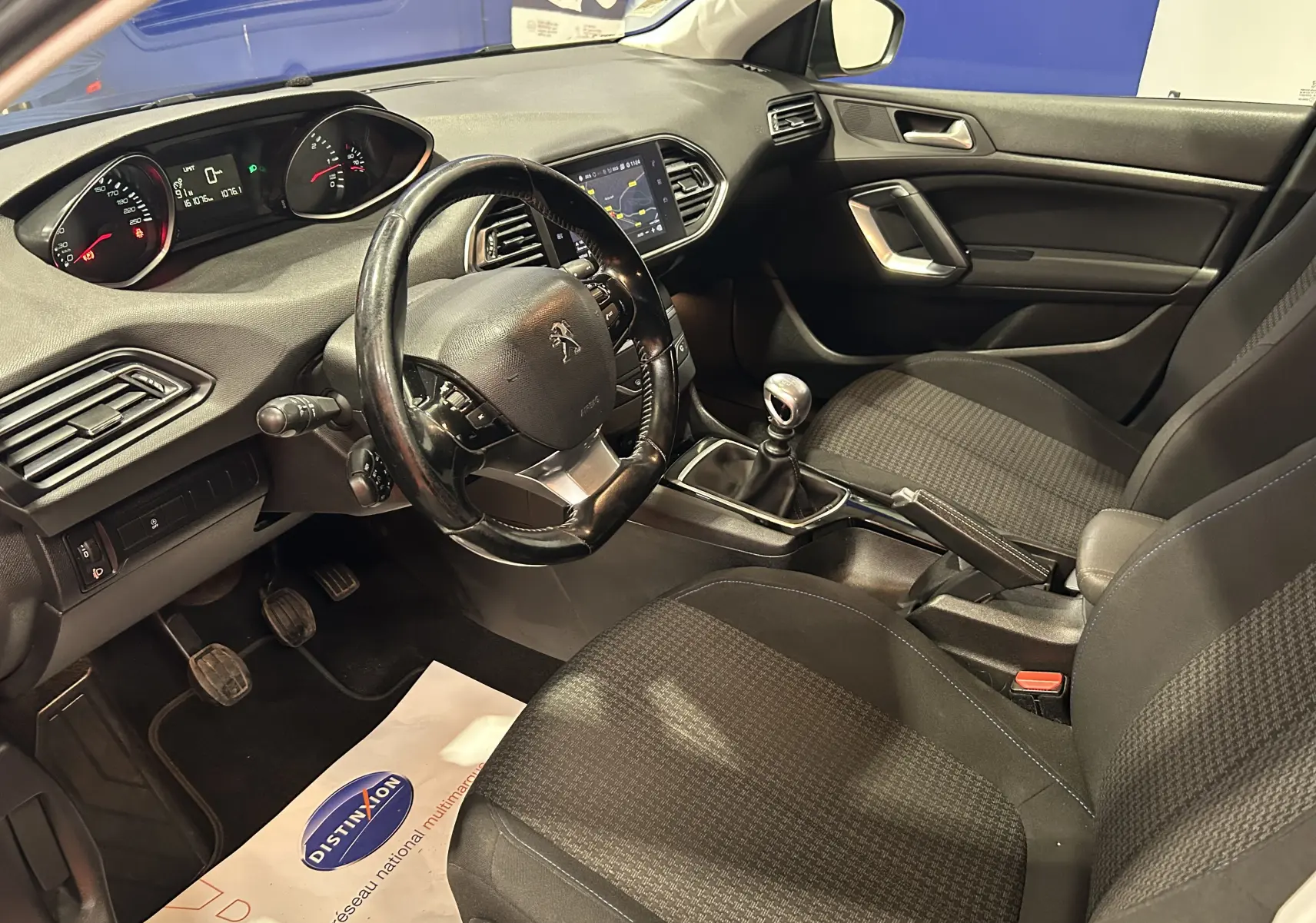 Vue intérieure côté conducteur de la Peugeot 308 SW noire, montrant le volant cuir, tableau de bord et levier de vitesses manuel.