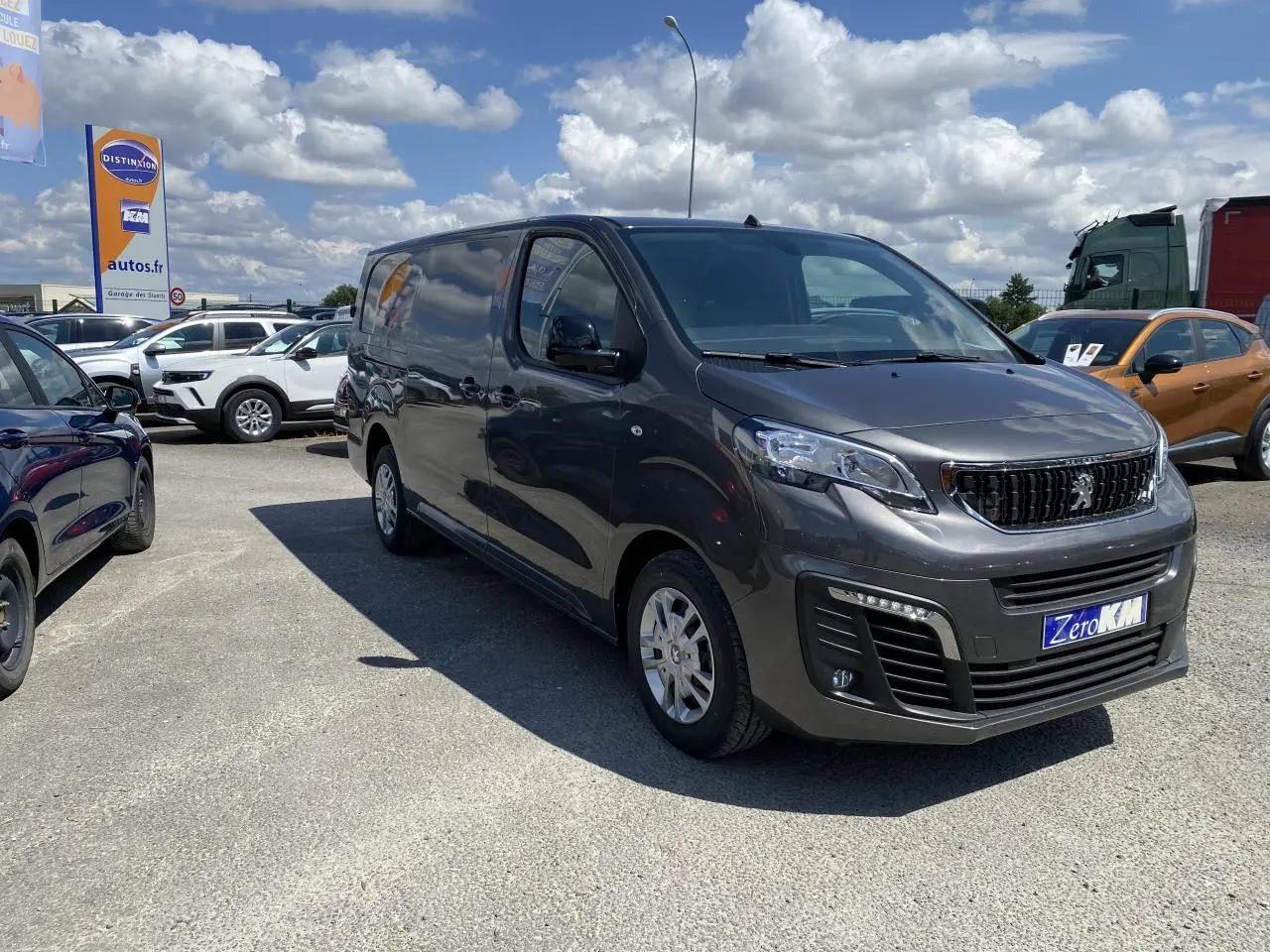 Peugeot Expert Fourgon gris platinium vu en 3/4 avant droit sur un parking sous ciel partiellement nuageux.