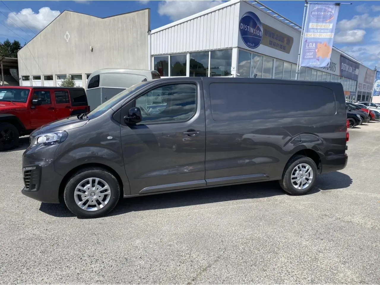 Vue de profil côté gauche d'un Peugeot Expert Fourgon gris platinium stationné devant un bâtiment commercial.