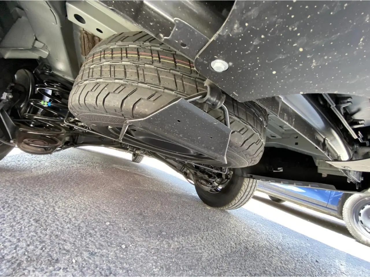 Vue en contre-plongée sous un Peugeot Expert Fourgon gris platinium, montrant la roue de secours suspendue sous le châssis.