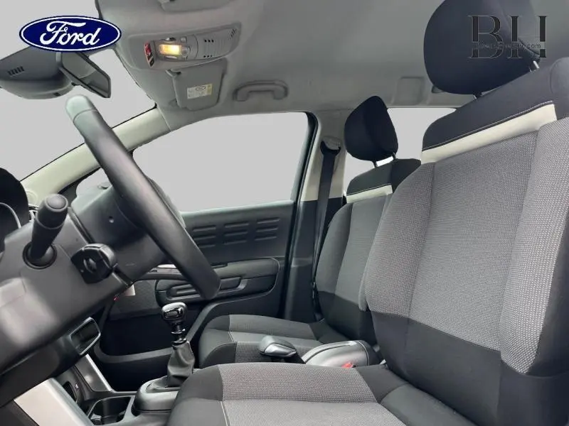 Intérieur vu côté conducteur d'une Citroën C3 Aircross blanc naturel avec sièges tissu gris et volant cuir noir.