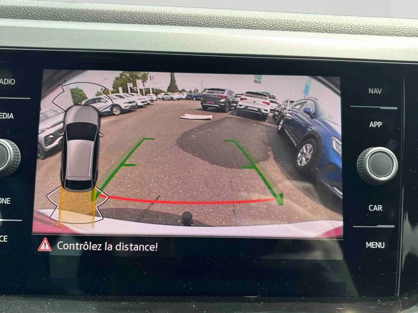Vue écran caméra de recul du Volkswagen Taigo blanc, avec guidage de trajectoire et alertes de distance visibles.
