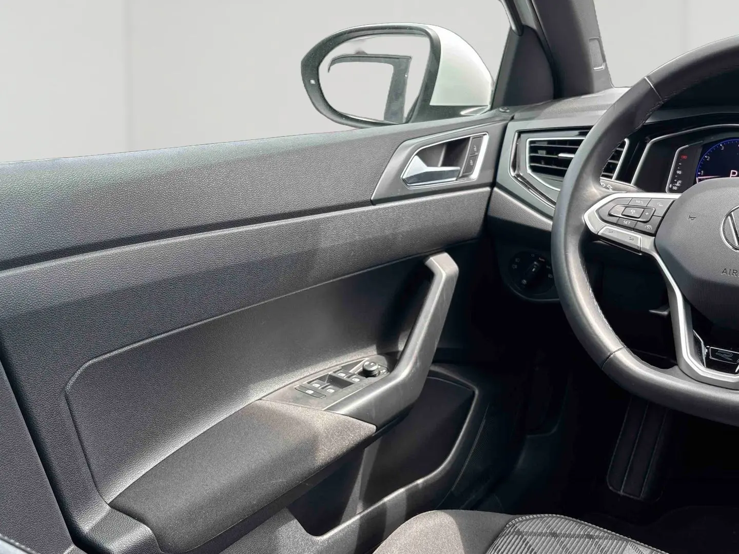Vue intérieure côté conducteur du Volkswagen Taigo 2025, montrant la portière noire et le volant cuir multifonctions avec logo R-Line.