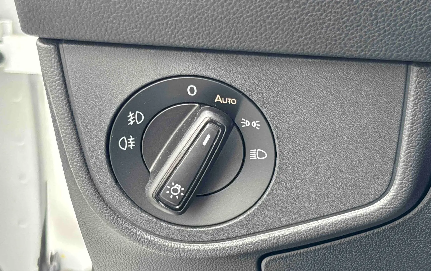 Gros plan sur le bouton de commande des phares dans l’habitacle du Volkswagen Taigo blanc, côté gauche.