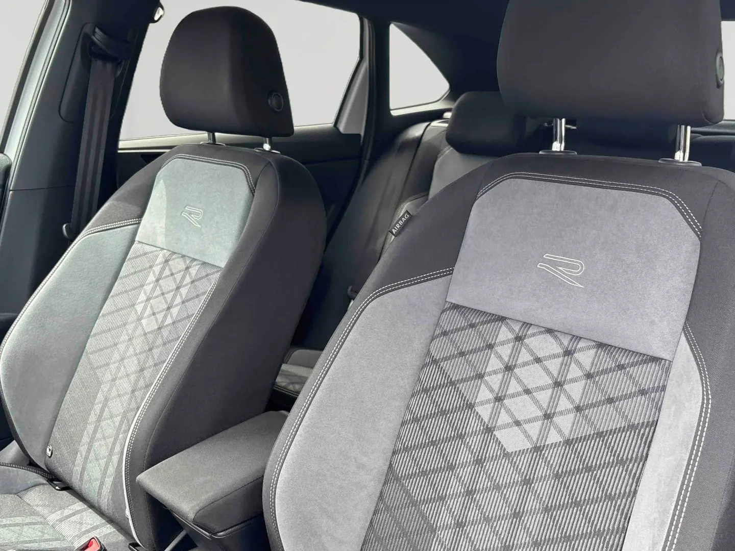 Gros plan sur les sièges avant gris et noirs avec logo R-Line brodé, intérieur du Volkswagen Taigo 2025.