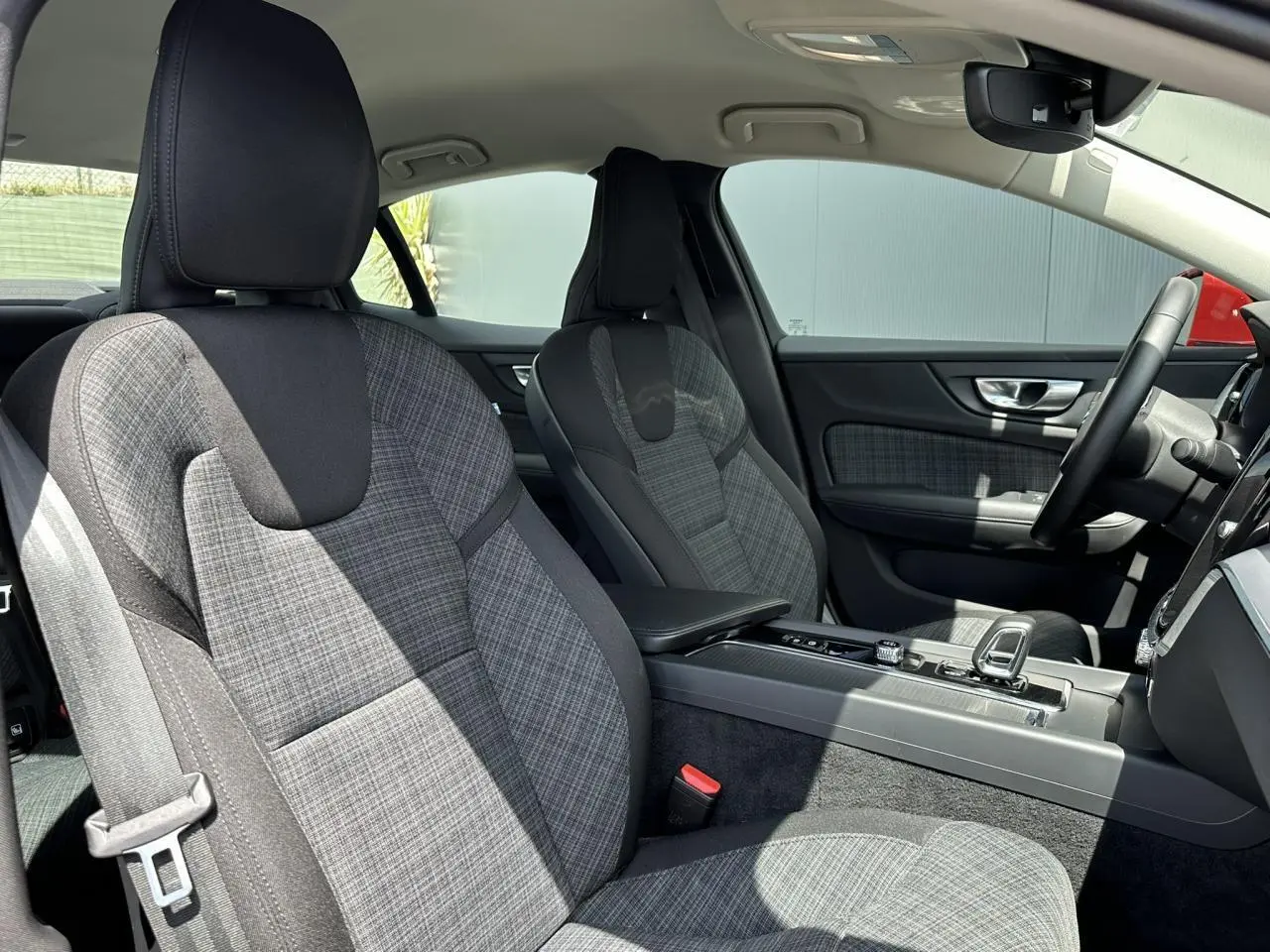 Intérieur avant de la Volvo S60 B4 2024, sièges tissu gris à motif carreaux, console centrale et volant visibles côté droit.