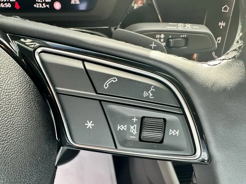 Gros plan sur les commandes vocales et audio au volant cuir noir de l'Audi A3 Sportback 2024 hybride.