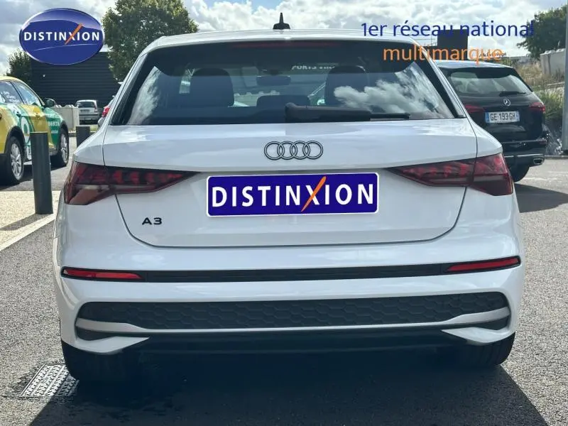 Vue arrière d'une Audi A3 Sportback blanche 2024 avec feux arrière LED et logo Audi visible sur un parking.