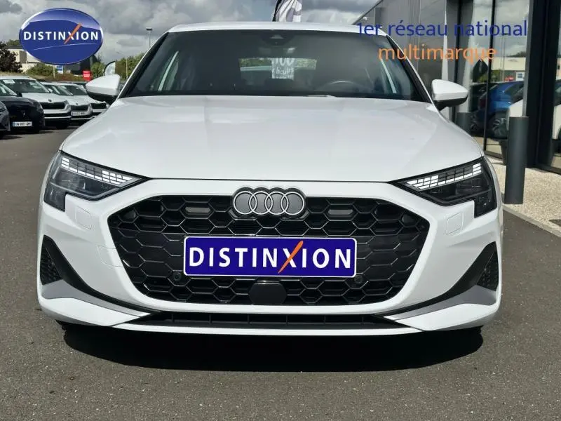 Vue frontale d'une Audi A3 Sportback blanche 2024 avec calandre noire hexagonale et phares LED distinctifs.