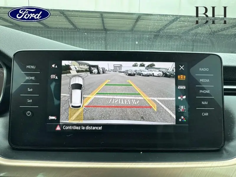 Écran tactile montrant la caméra de recul d'une Skoda Kamiq gris graphite, avec lignes d'aide au stationnement visibles.