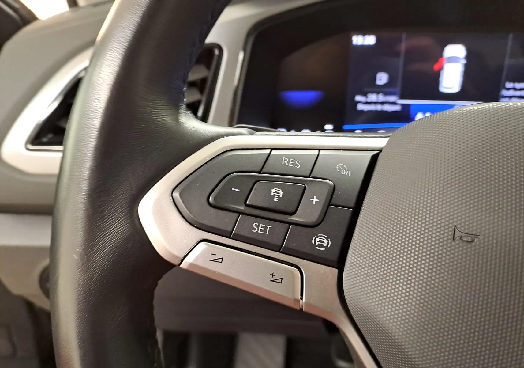 Gros plan sur les commandes au volant du Volkswagen T-Roc 2024, mettant en valeur les boutons de régulateur de vitesse et l'écran numérique en arrière-plan.