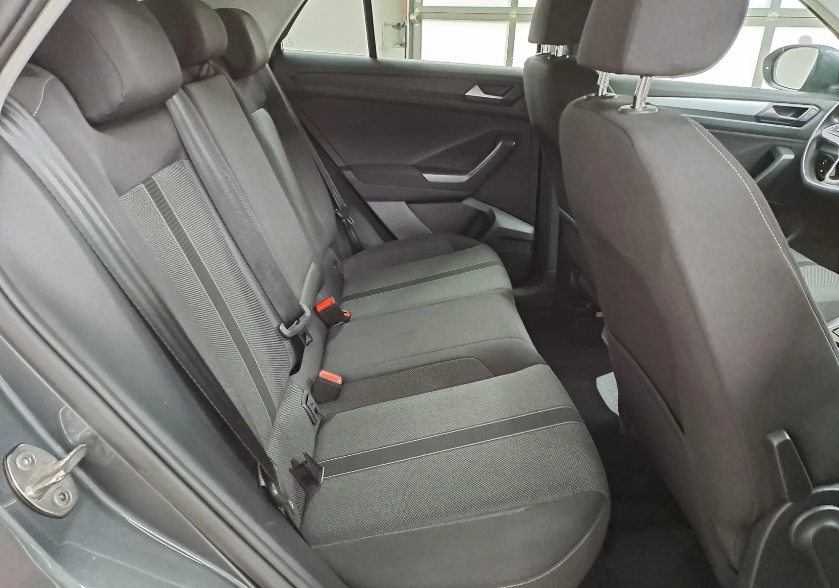 Vue intérieure du siège arrière droit du Volkswagen T-Roc 2024, tissu noir avec détails gris, portes ouvertes.