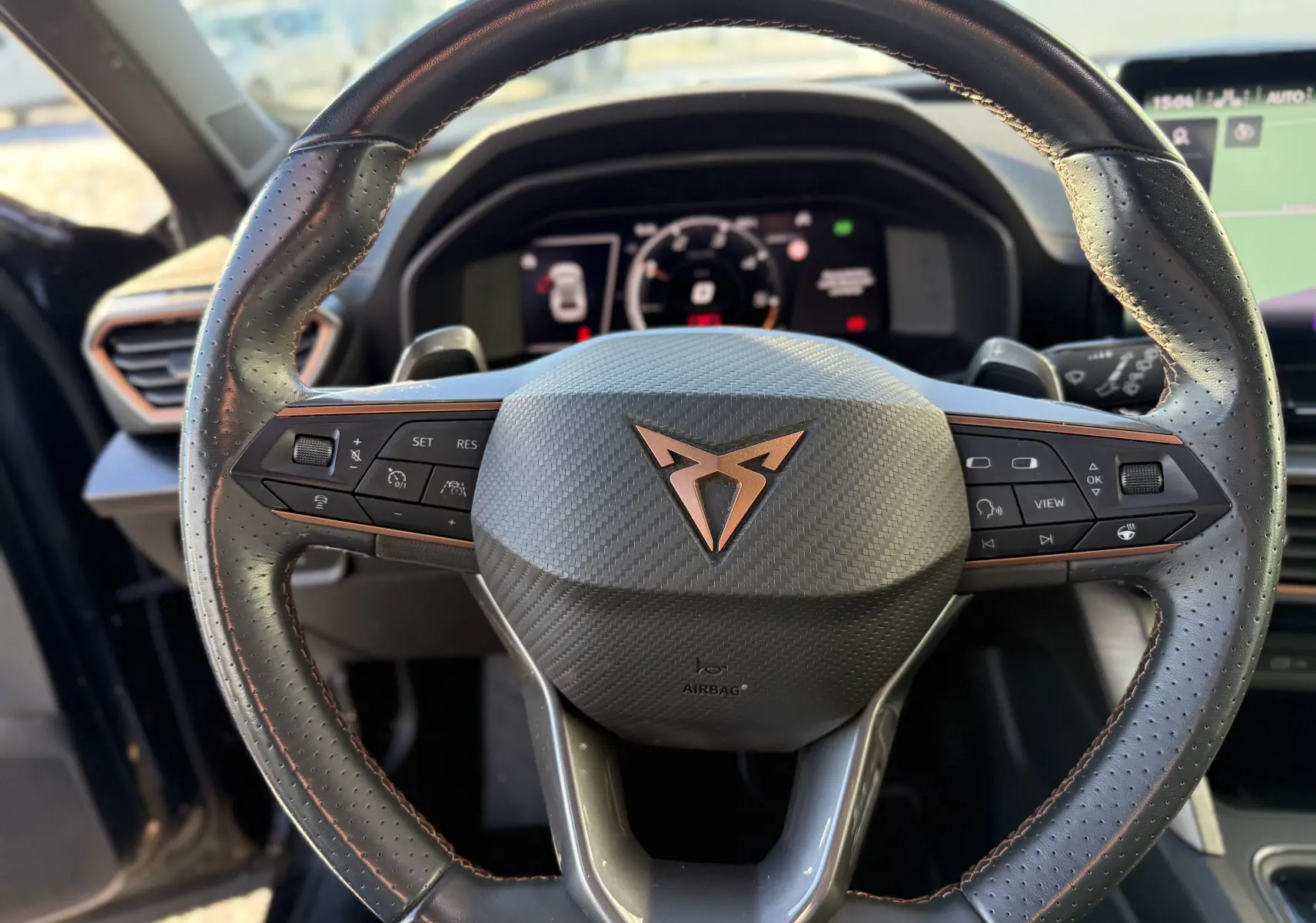 Vue rapprochée du volant en cuir noir perforé avec logo CUPRA cuivré du SUV Formentor 2023, tableau de bord numérique en arrière-plan.