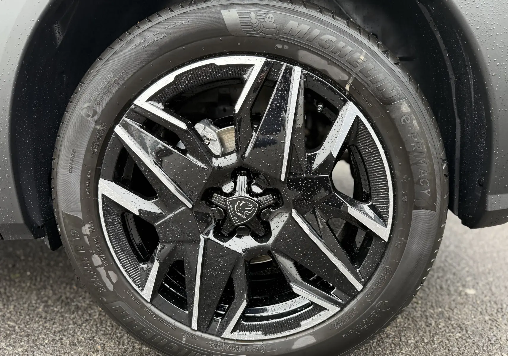 Gros plan sur la jante noire et argentée du Peugeot 3008 Hybrid 2025, avec logo lion au centre et pneus Michelin mouillés.