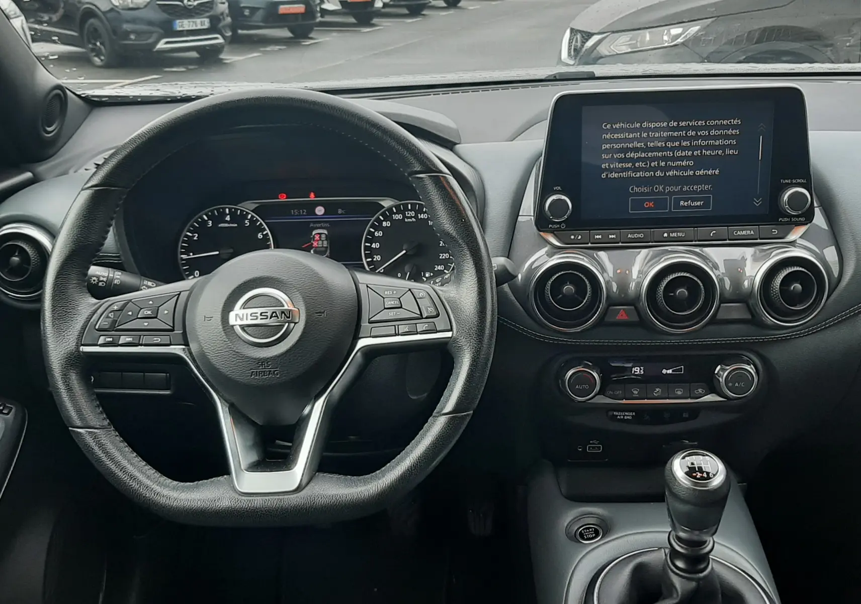 Vue intérieure centrée sur le volant et la console d'une Nissan Juke gris, avec boîte manuelle et écran tactile allumé.