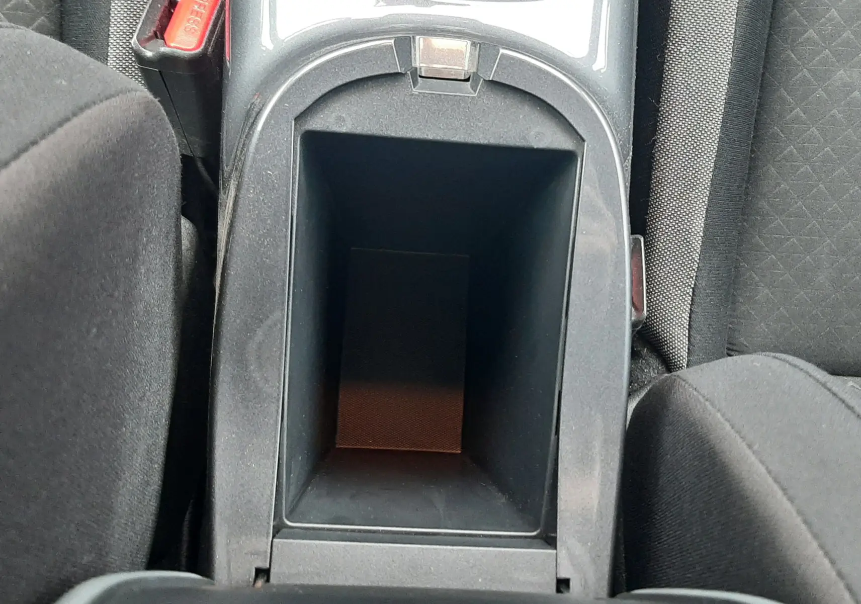 Vue plongeante sur le rangement central noir entre les sièges avant du Nissan Juke gris, avec porte-gobelets et ceinture de sécurité visible.