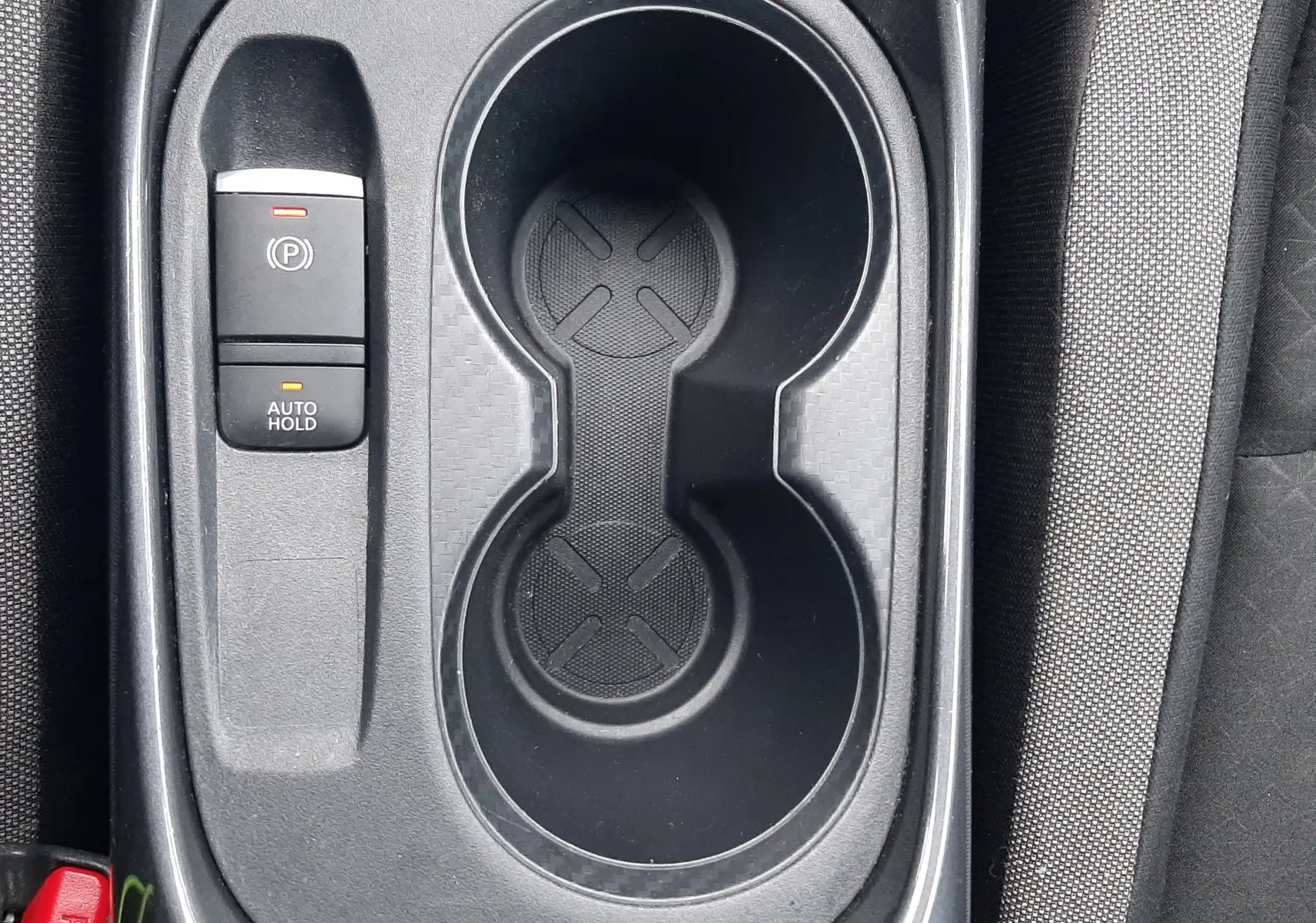 Gros plan sur la console centrale noire du Nissan Juke 2020, avec porte-gobelets et bouton frein à main électrique.