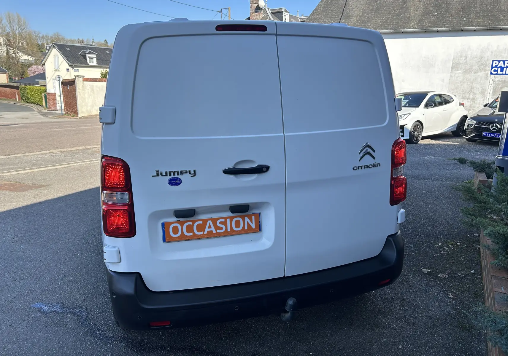 Vue arrière d'un fourgon blanc Citroën Jumpy avec attelage et plaque "OCCASION" en environnement urbain.