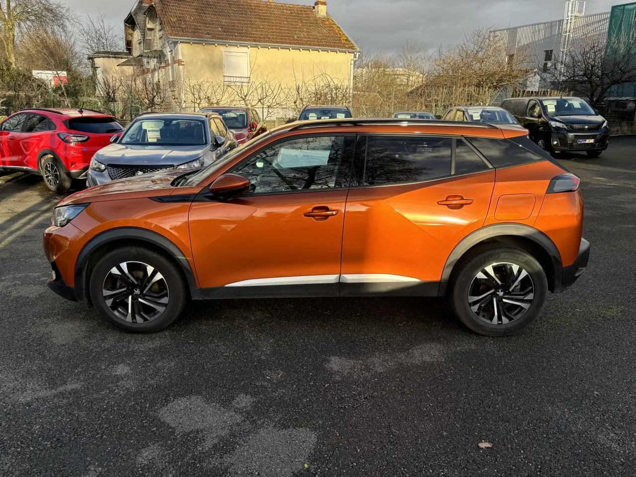 Profil droit d’un Peugeot 2008 2021 en peinture métallisée Orange Fusion, soulignant ses lignes anguleuses et ses jantes noires.