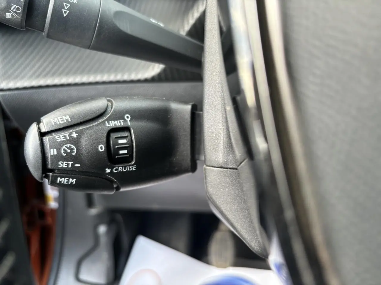 Gros plan sur la commande de régulateur de vitesse à gauche du volant dans l’habitacle du Peugeot 2008 Orange Fusion.