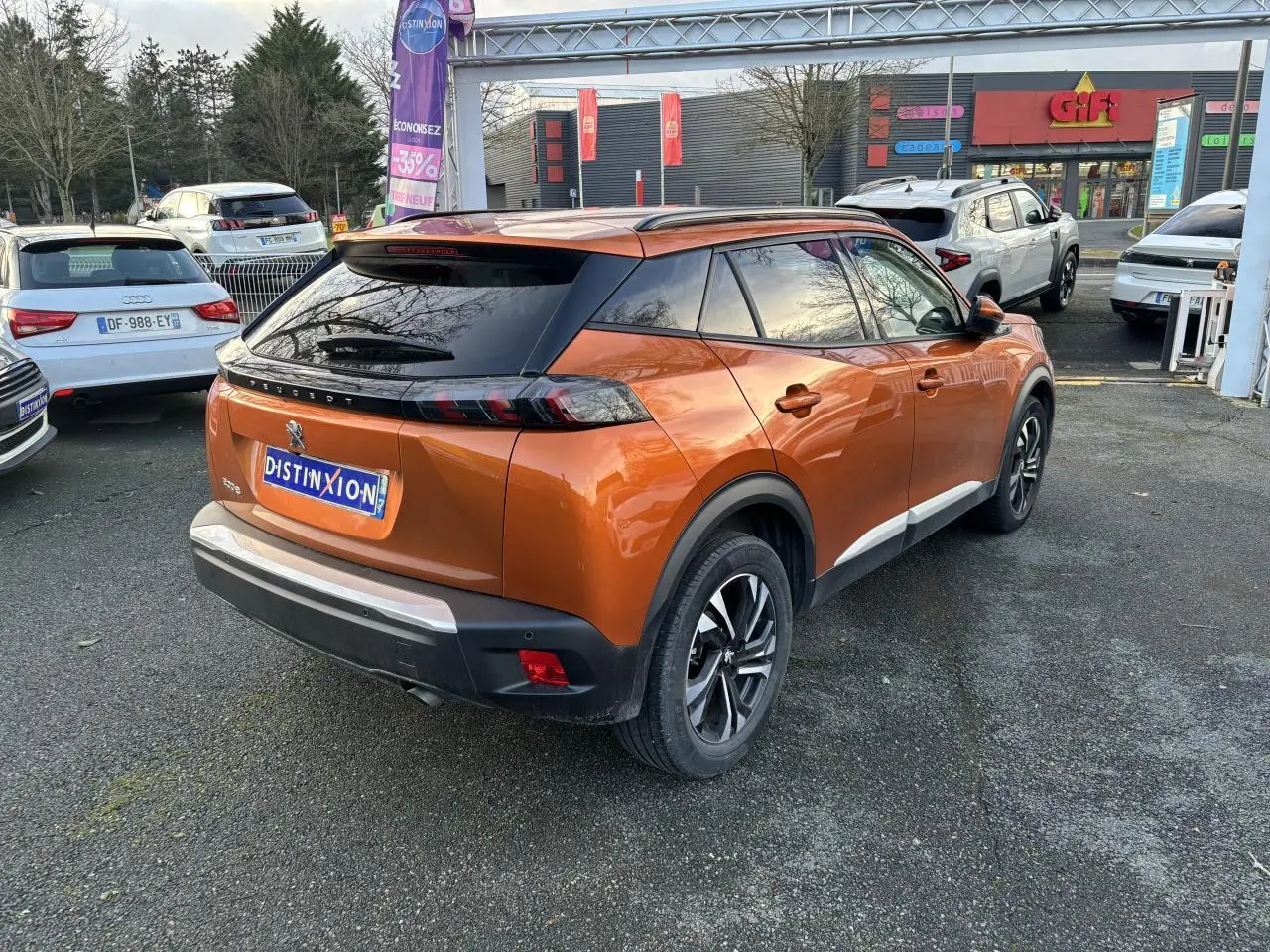 Vue 3/4 arrière droite d’un Peugeot 2008 orange fusion avec toit noir et jantes alliage bicolores sur parking.