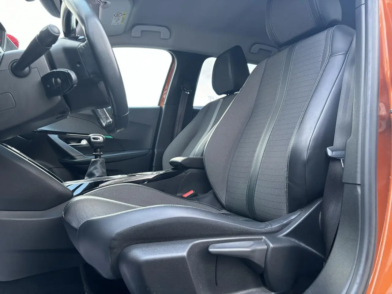 Vue intérieure côté conducteur du siège avant en tissu et cuir noir, avec porte orange fusion visible en arrière-plan.