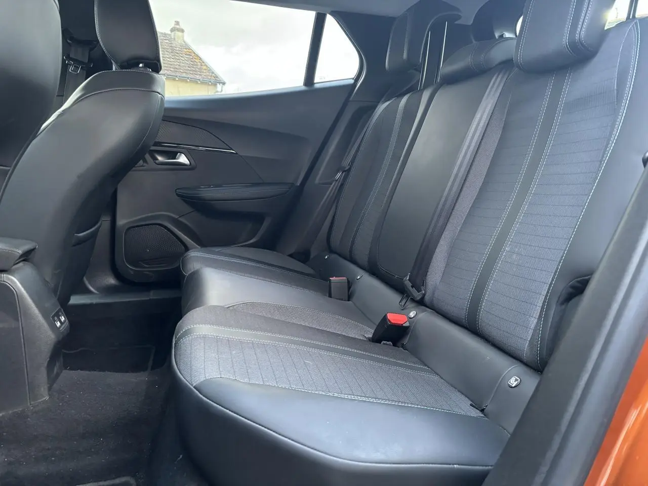Vue intérieure de la banquette arrière côté droit de la Peugeot 2008 orange fusion, avec sièges en tissu et cuir noir.