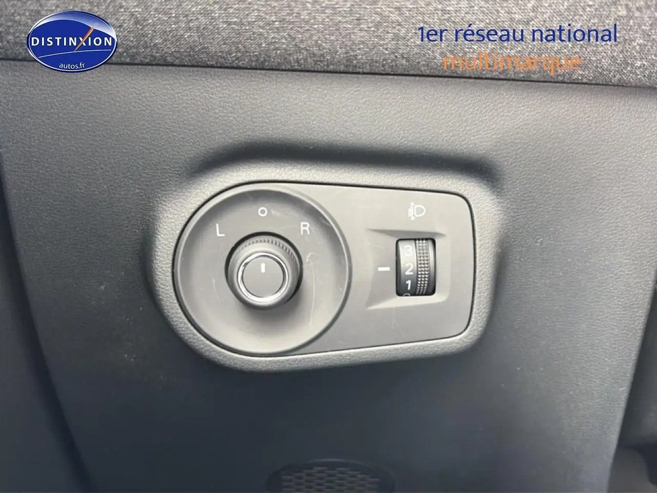 Gros plan sur les commandes grises de réglage des rétroviseurs et des phares du MG ZS Hybrid blanc, côté conducteur.