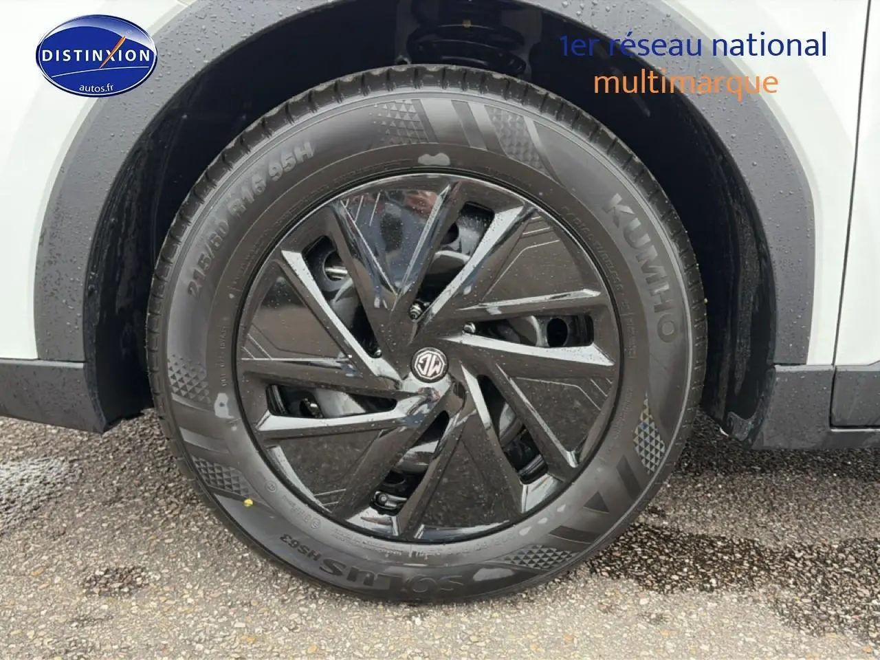 Gros plan sur la roue avant droite noire et brillante du MG ZS Hybrid blanc, avec logo MG au centre.